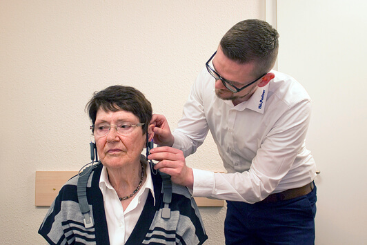 Ein Hörakustiker prüft das Hörvermögen einer älteren Frau mit einem Hörtestgerät.