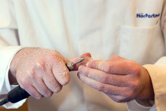 Ein Hörakustiker schleift ein Hörgerät individuell für den optimalen Hörkomfort zurecht.